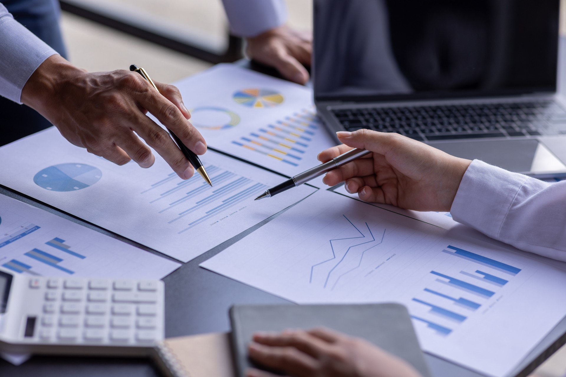 Team businesspeople or an accountant team are analyzing data charts, graphs, and a dashboard on a laptop screen in order to prepare a statistical report and discuss financial data in an office.